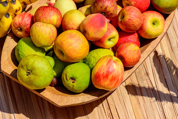 Wooden bowl and rustic straw mat with various guavas, apples and bananas under the sunlight