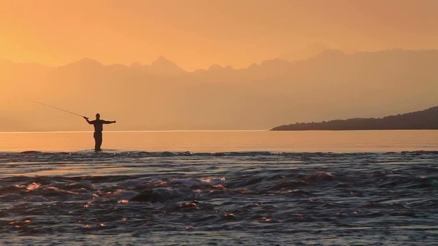 Fisherman fly fishing at sunset at the lake and mountains