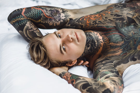 Young handsome tattooed man laying in bed in the open air outdoors in the garden.