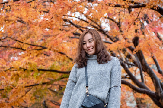 Portrait image of beautiful asian woman enjoyed standing in the garden with red and orange tree leaves in autumn background