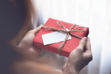 Young woman hands holding red gift box with blank card for Valentines day, copy space.