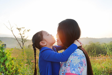 Close up asian mother and daughters kissing in the meadow field at morning sunrise.