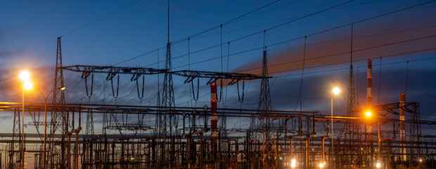 Electrical substation at night,in the background smoking power plant chimneys