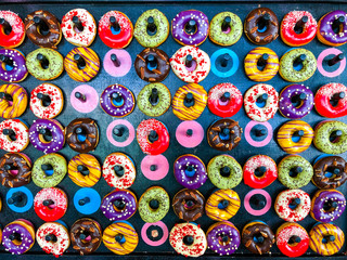 Various decorated doughnuts hung on a black background. Sweet and colorful doughnuts arranged on a board.