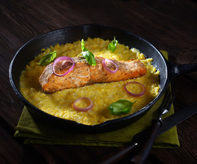 baked salmon steak  in a pan on a corn palette with basil on a wooden background. rustic style.