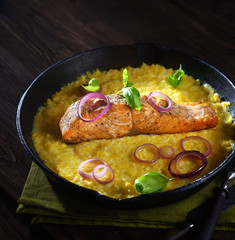 baked salmon steak  in a pan on a corn palette with basil on a wooden background. rustic style.