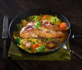 baked salmon steak  in a pan on a corn palette with basil on a wooden background. rustic style.