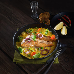 baked salmon steak  in a pan on a corn palette with basil on a wooden background. rustic style.