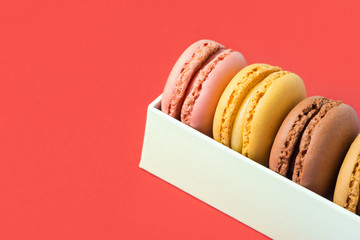 Variety of multicolored different flavors pink chocolate coffee yellow mocha macarons in white gift box on coral background. Bakery confectionery pastry shop poster banner template. Valentine desert