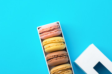 Variety of multicolored different flavors pink chocolate coffee yellow mocha macarons in white gift box with lid on mint blue background. Bakery confectionery pastry shop poster banner template