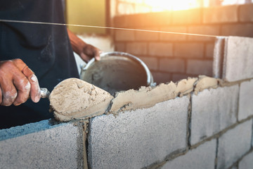 Worker building wall bricks with cement - obrazy, fototapety, plakaty