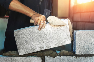 Worker building wall bricks with cement - obrazy, fototapety, plakaty