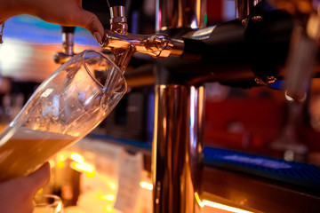Hand of bartender pouring a large lager beer in tap.