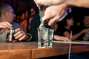 Barman pouring hard spirit into glasses in detail