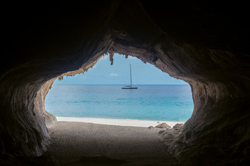 Fototapeta na wymiar Exit from the cave overlooking beautiful sea and boat at Cala Luna beach