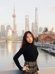 Beautiful young brunette woman in black clothes posing with blur Shanghai Bund landmark buildings background in autumn dusk light.  Emotions, people, beauty, travel and lifestyle concept.