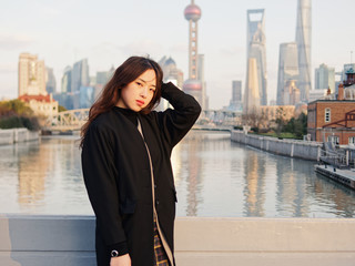 Beautiful young brunette woman in black clothes posing with blur Shanghai Bund landmark buildings...