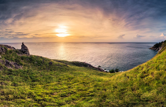 Sunset over horizon on ocean with green hill