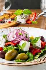 Greek salad with feta cheese, olives and herbs, served in a white plate on a table in a restaurant.