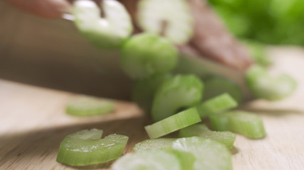 Woman preparing food in her kitchen, she is chopping fresh celery on a cutting board with a knife