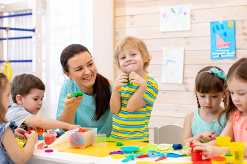 Children dough play in daycare centre. Kids with teacher mold from plasticine in kindergarten. Little students knead modeling clay with hands in preschool.
