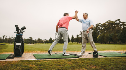 Senior golfers high five at driving range