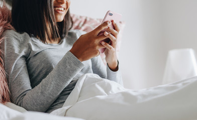 Happy girl sitting on bed using mobile phone