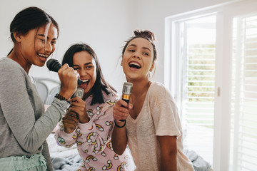 Happy girls singing karaoke during a sleepover - obrazy, fototapety, plakaty