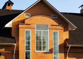 Facade of brick mansion with three rectangular windows, chimney and multilevel roof, closeup