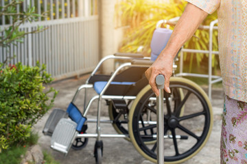 Asian old woman standing with his hands on a walking stick,Hand of old woman holding a staff cane with wheelchair background