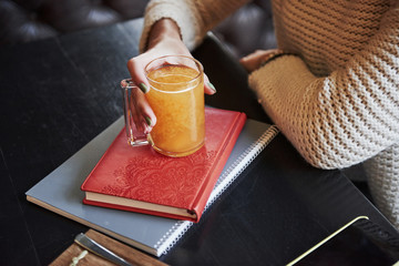 Close up photo of the orange drink that holds by woman hand and stands on the book with red cover