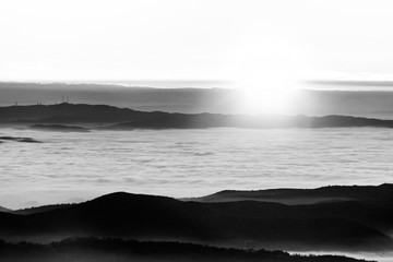 Beautiful sunset over a valley filled by fog with mountains and hills