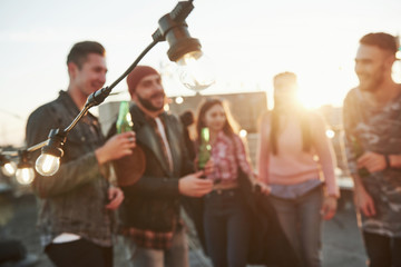 Blurred people. Close up view of the wire with light bulbs with young friends with bottles on background