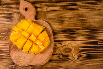 Cutting board with chopped mango fruit on a wooden table. Top view