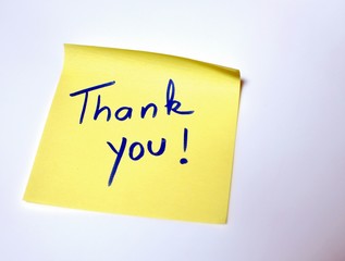 The sentence Thank you written by hand on a yellow post it and put on the white table