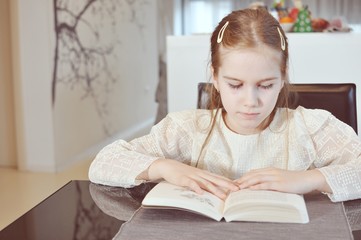 White Caucasian girl (child, kid) sitting at the table and read a book