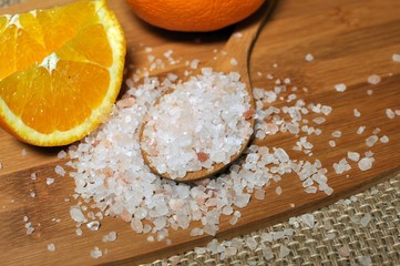 Concept of wooden spoon full of Himalayan pink salt with a slice of orange in background