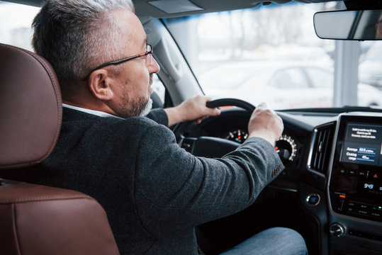 Looking Into The Front Mirror. View From Behind Of Senior Businessman In Official Clothes Driving A Modern New Car