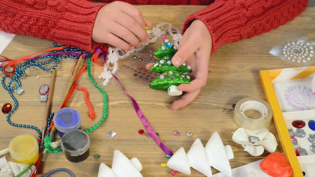 
Child girl is making decoration for holidays. Crafts and toys, christmas tree and other. Painting watercolors. Top view. Artwork workplace with creative accessories. Flat lay art tools.