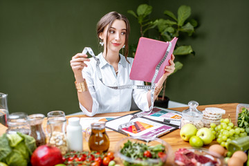Woman dietitian in medical uniform working on a diet plan sitting with different healthy food ingredients in the green office