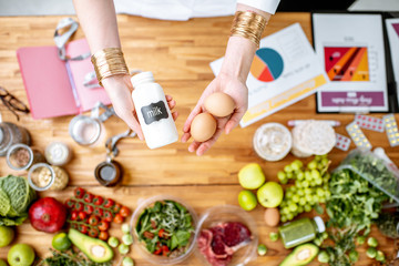 Dietitian holding milk and eggs above the table full of various healthy products and drawings on the topic of healthy eating