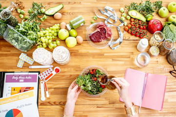 Dietitian working on a healthy diet pouring olive oil into the salad at the table full of various...