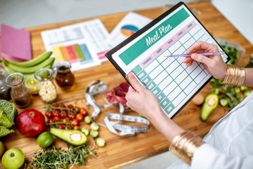 Dietitian writing a diet plan, view from above on the table with different healthy products and drawings on the topic of healthy eating