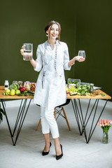 Full body portrait of a young woman nutritionist in medical gown standing with water in the office...