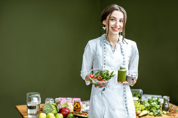 Portrait of a young woman nutritionist in medical gown standing with salad and smoothie on the...