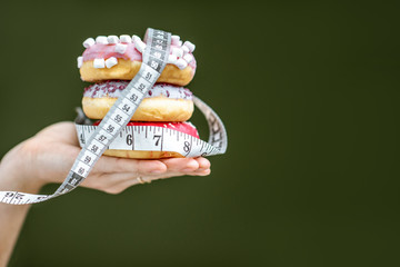 Three sweet donuts covered with measurement tape on the hand on the green background. Unhealthy...