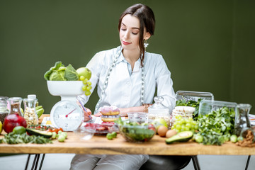 Woman dietitian in medical uniform working on a diet plan sitting with various healthy food ingredients in the green office