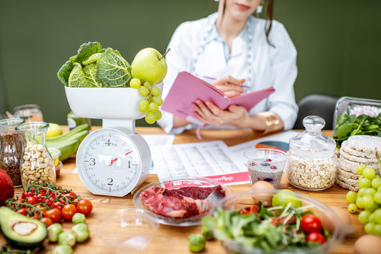 Woman dietitian working on a diet plan sitting with various healthy food ingredients, cropped image focused on food