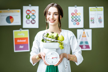 Young woman nutritionist in medical gown holding weights full of healthy products standing on the...