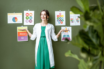 Portrait of a woman dietitian in medical gown standing on the green wall background with drawings...